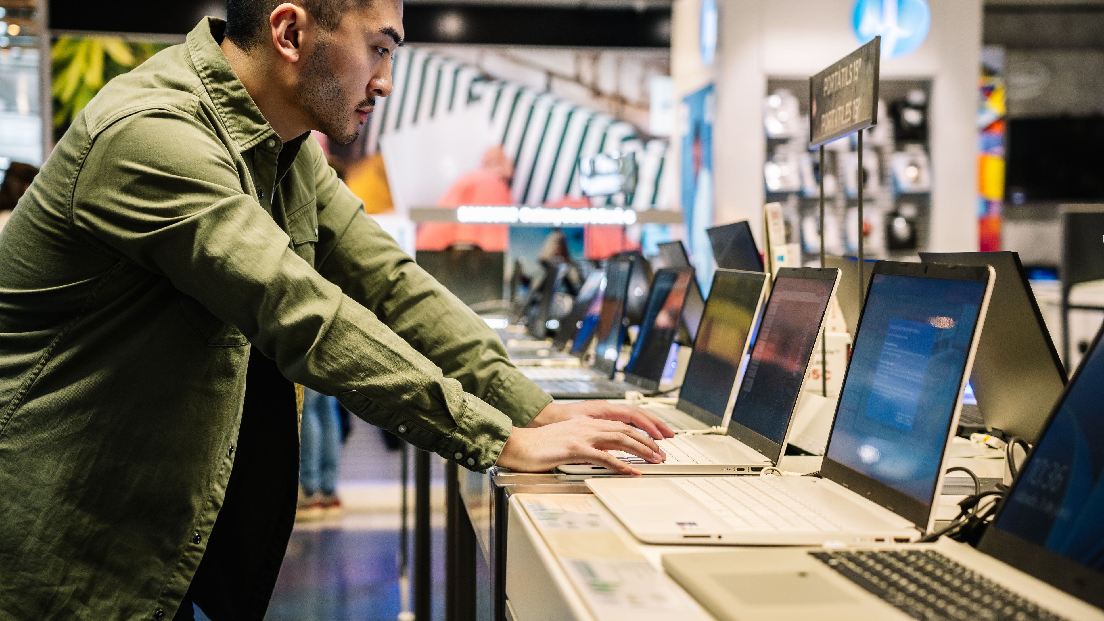 A man browsing and testing laptops in an electronics store.