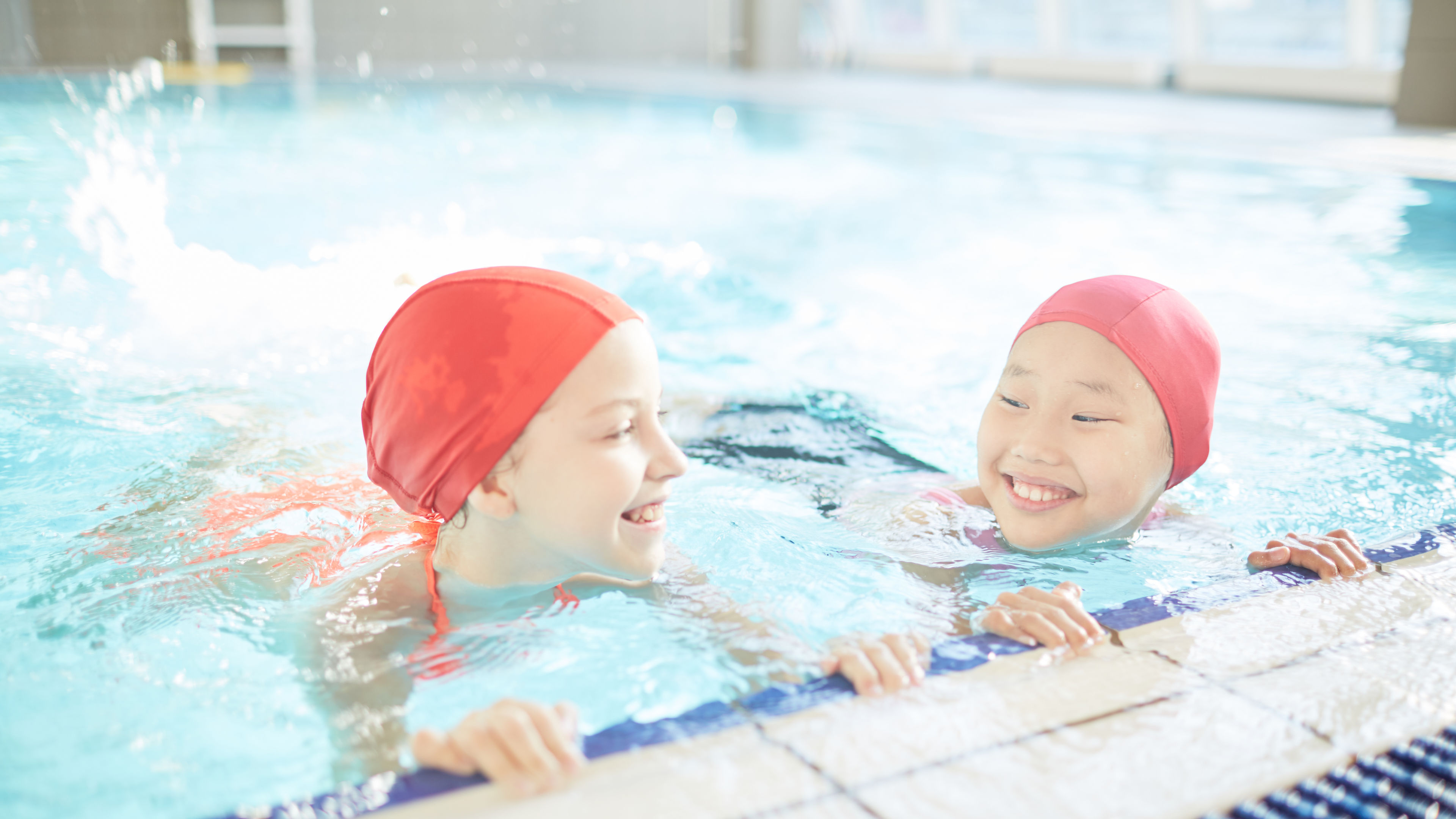 Two friendly girls having fun while practicing swimming in pool