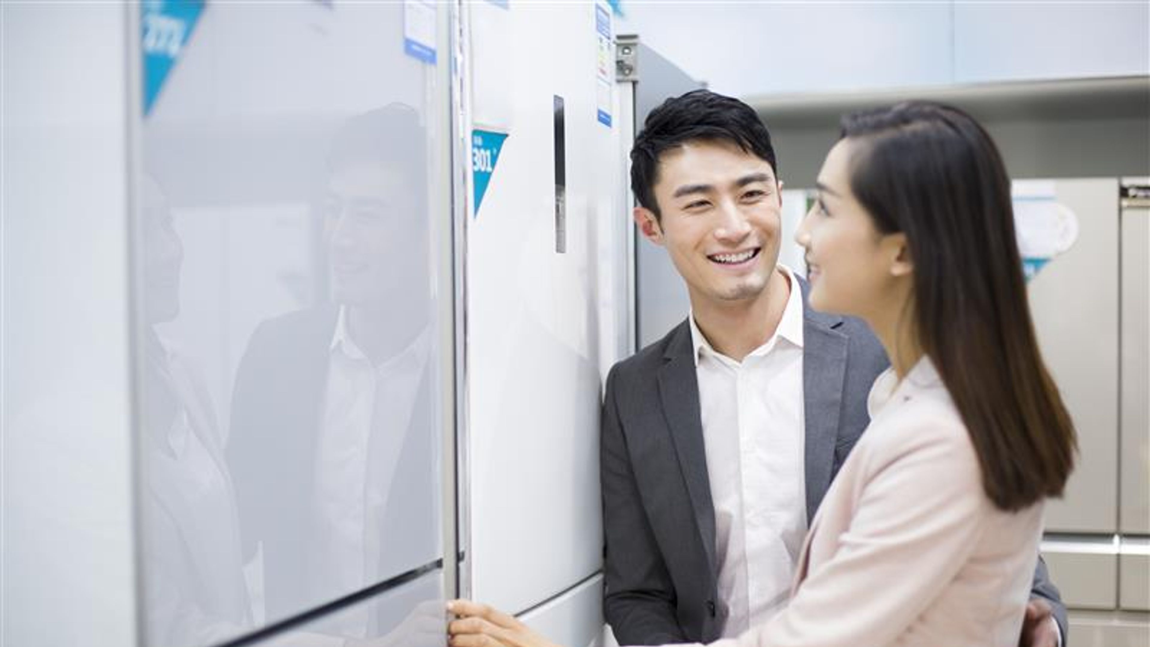 Two people smiling and looking at the refrigerator.